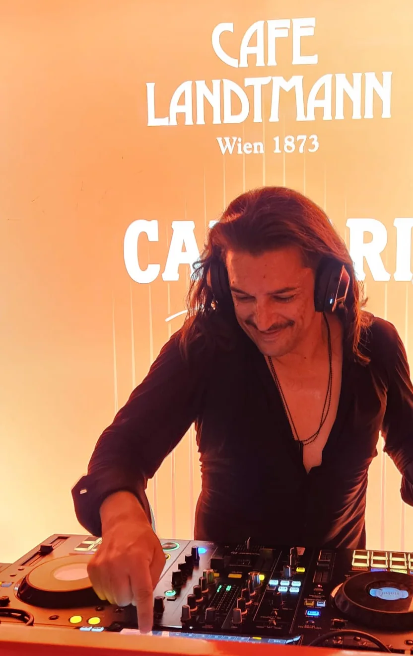 Steve Manera mit Kopfhörern an einem DJ-Pult, hinter ihm der Schriftzug des Café Landtmann.
